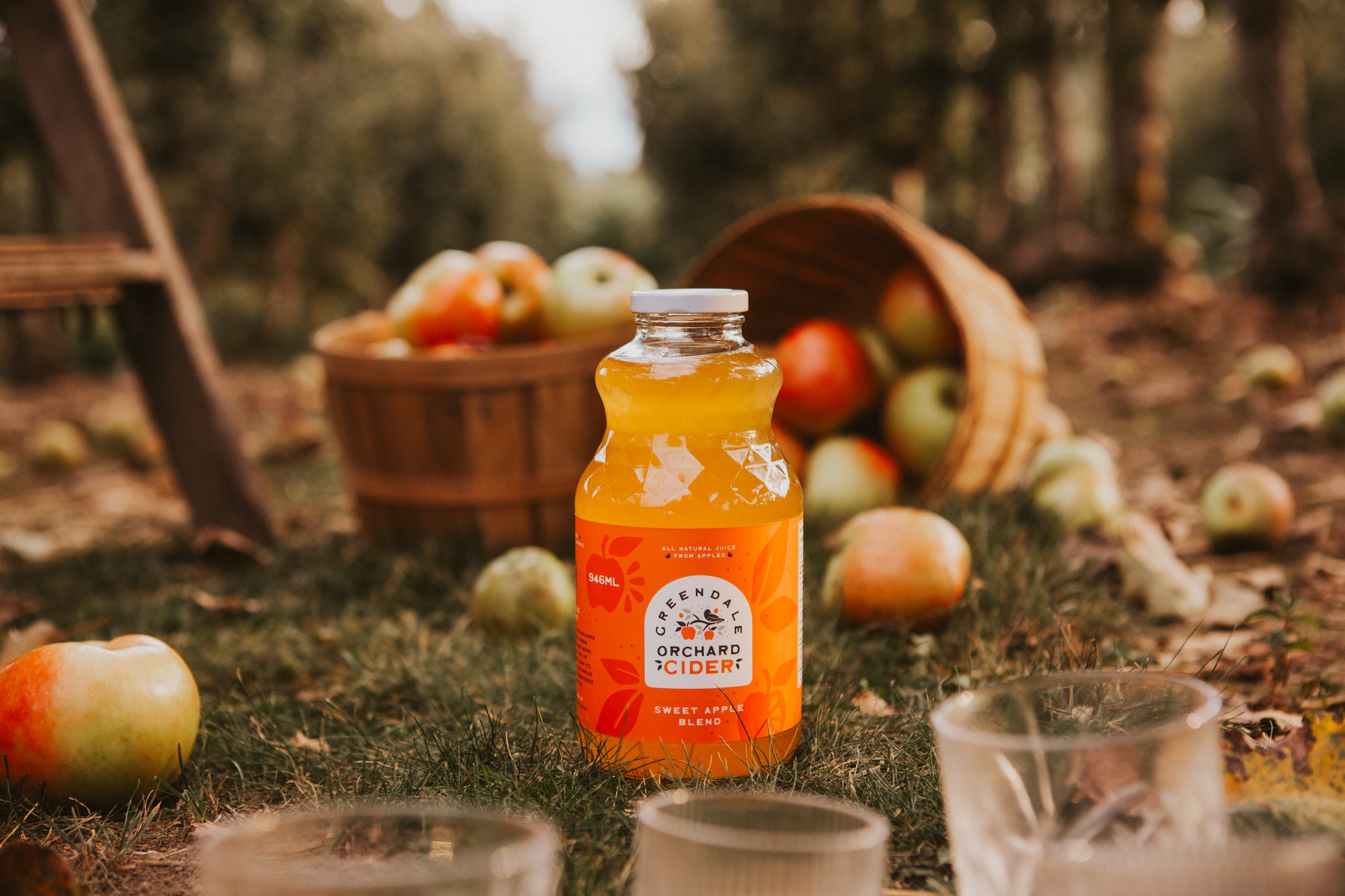 Bottle of Orchard Cider with apples and a wooden barrel in an outdoor setting