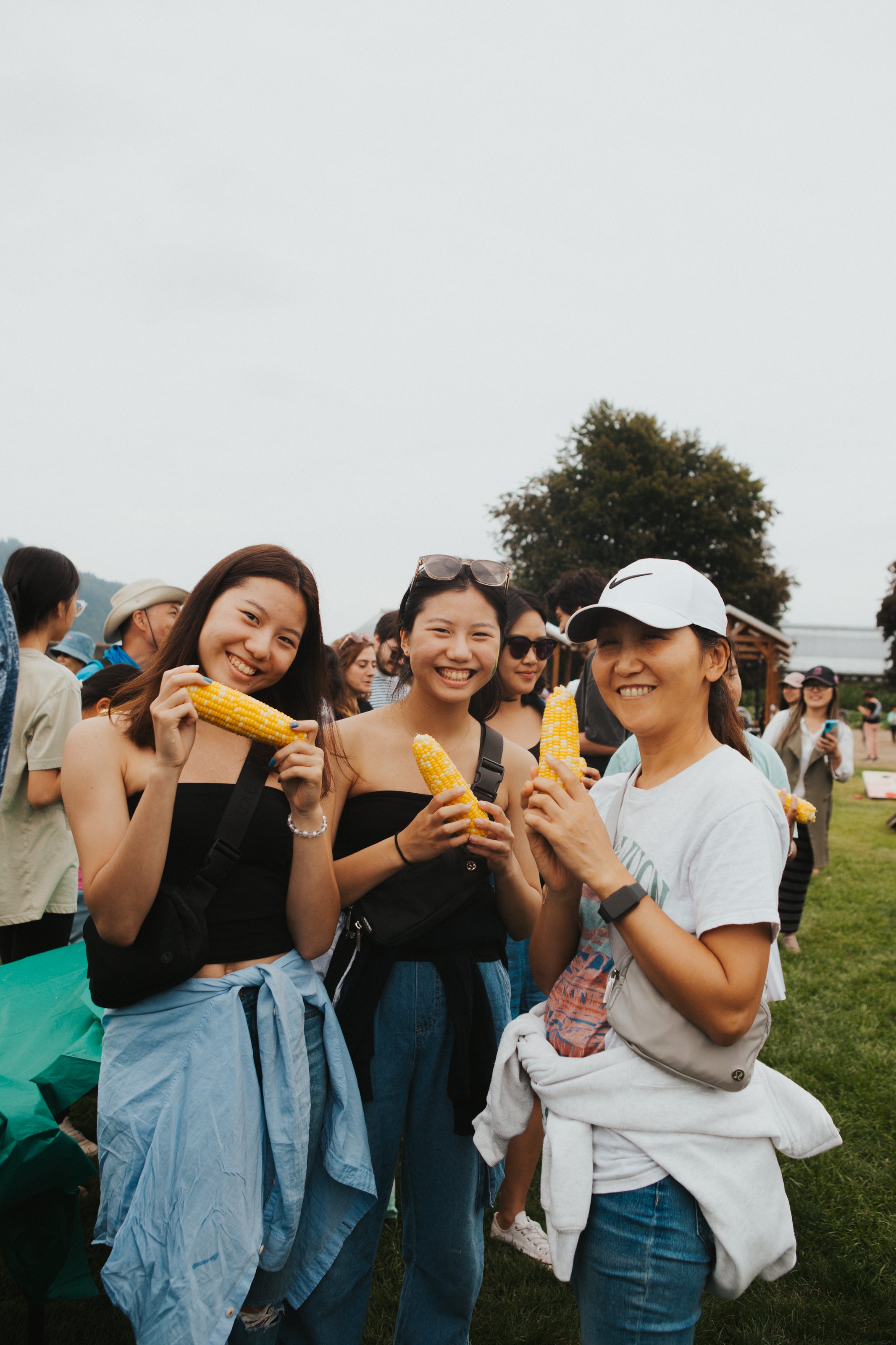 Three women holding corn on the cob outdoors with a casual setting